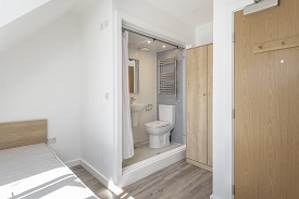 An en suite bedroom in Old Vicarage with bed on the left hand side. The entrance to the en suite is in the middle of the frame with a toilet, a towel rail above the toilet, a sink and mirror. A cupboard is to the right of the en suite.